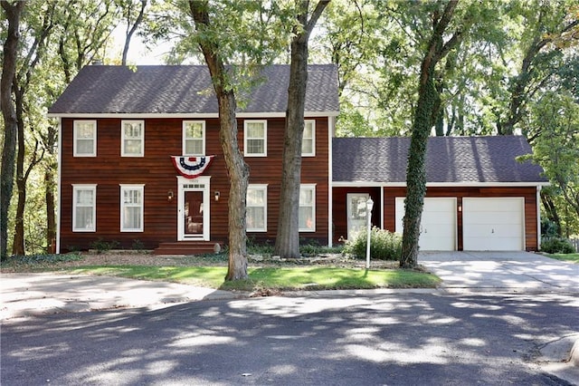 colonial inspired home featuring an attached garage, concrete driveway, and roof with shingles