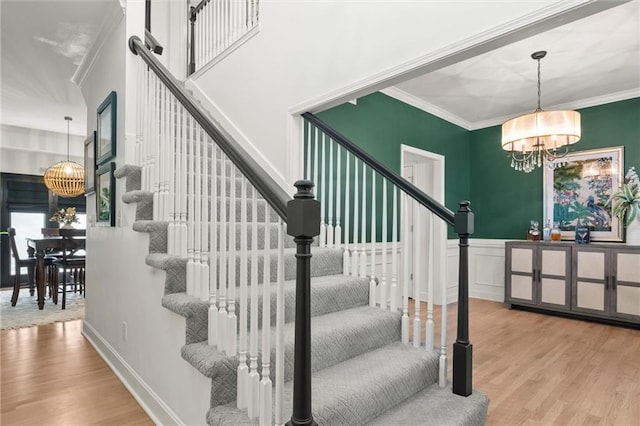 staircase with ornamental molding, a notable chandelier, and hardwood / wood-style floors