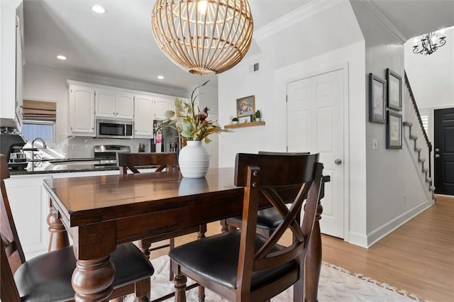 dining room with crown molding, an inviting chandelier, sink, and light hardwood / wood-style floors