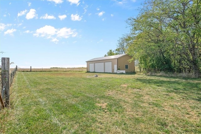 view of yard featuring a rural view, a garage, and an outbuilding