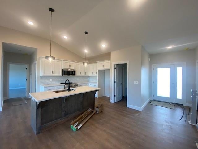 kitchen featuring light countertops, stainless steel microwave, a kitchen island with sink, a sink, and white cabinetry