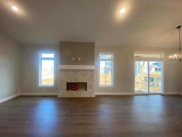 unfurnished living room featuring a fireplace, a chandelier, dark wood-style flooring, and a wealth of natural light