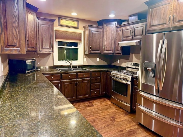 kitchen with sink, hardwood / wood-style flooring, stainless steel appliances, and dark stone counters