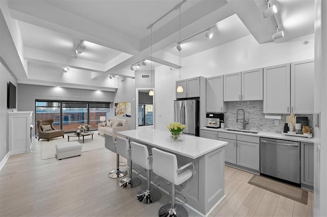 kitchen featuring gray cabinetry, appliances with stainless steel finishes, hanging light fixtures, sink, and a breakfast bar area