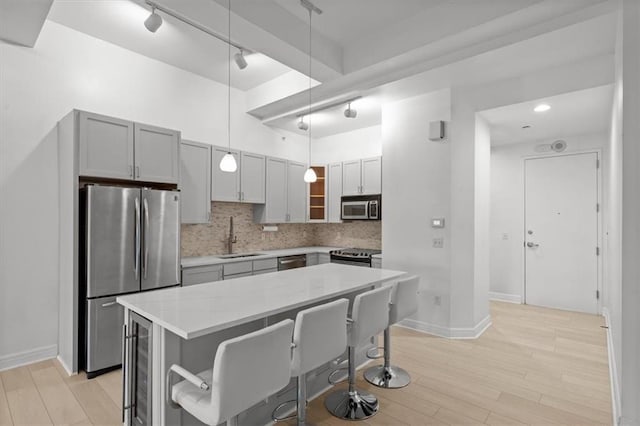 kitchen with stainless steel appliances, sink, light wood-type flooring, a kitchen island, and pendant lighting