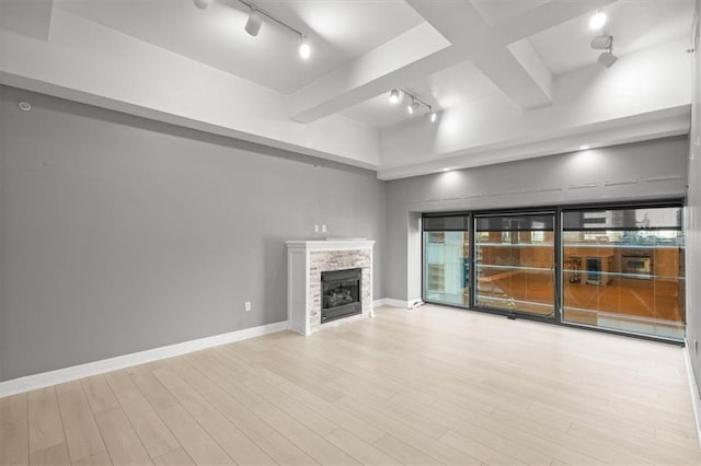 unfurnished living room featuring beam ceiling, track lighting, light hardwood / wood-style floors, and a fireplace