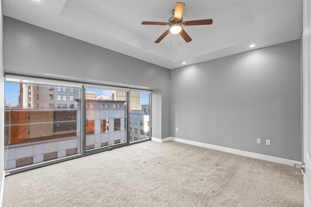 carpeted empty room with ceiling fan and a raised ceiling