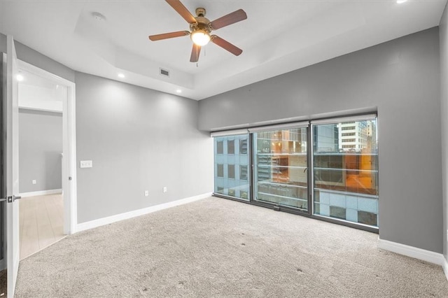 carpeted empty room with ceiling fan and a raised ceiling