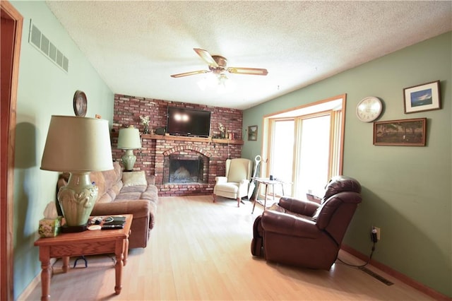 living room with ceiling fan, a textured ceiling, light hardwood / wood-style flooring, and a brick fireplace