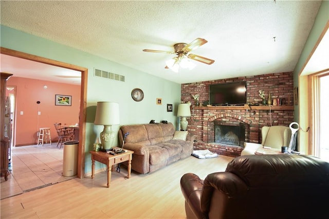 living room featuring a textured ceiling, a fireplace, light hardwood / wood-style floors, and ceiling fan