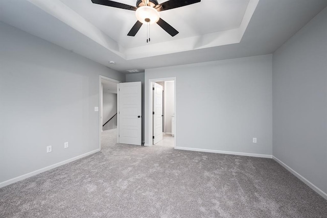 unfurnished bedroom with a raised ceiling, connected bathroom, ceiling fan, and light colored carpet