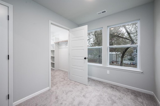 unfurnished bedroom featuring a walk in closet, a closet, and light colored carpet