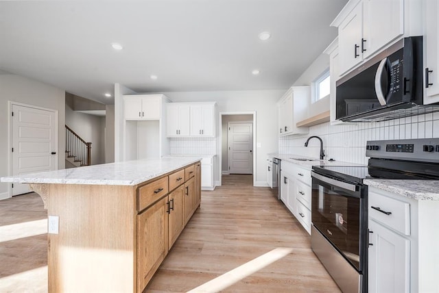 kitchen featuring light wood-type flooring, appliances with stainless steel finishes, a kitchen island, light stone counters, and white cabinetry