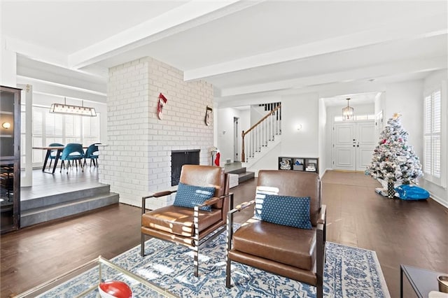 living room featuring beamed ceiling, dark hardwood / wood-style flooring, a brick fireplace, and a wealth of natural light