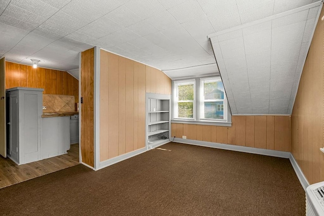 additional living space featuring lofted ceiling, wooden walls, and dark carpet