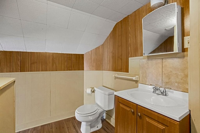 bathroom featuring wood-type flooring, vaulted ceiling, toilet, wood walls, and vanity