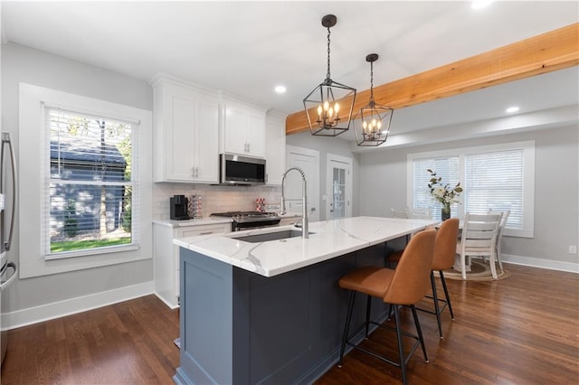 kitchen with a kitchen island with sink, dark hardwood / wood-style floors, stainless steel appliances, pendant lighting, and white cabinetry