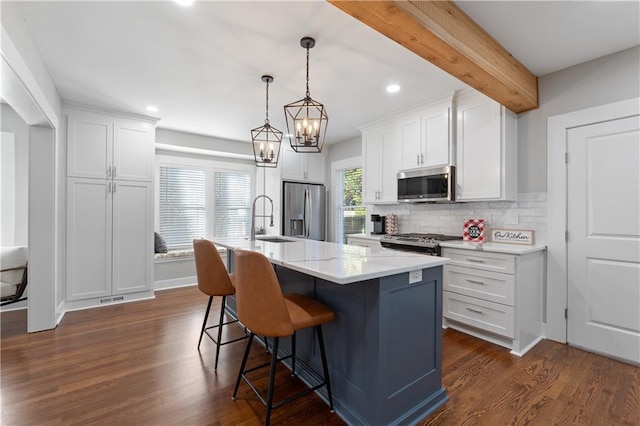 kitchen with appliances with stainless steel finishes, dark hardwood / wood-style flooring, white cabinetry, pendant lighting, and a kitchen island with sink