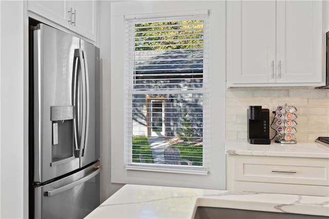 kitchen featuring stainless steel fridge, white cabinets, light stone countertops, and tasteful backsplash