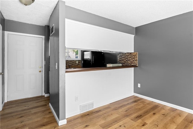 kitchen with black refrigerator, hardwood / wood-style floors, a textured ceiling, and tasteful backsplash