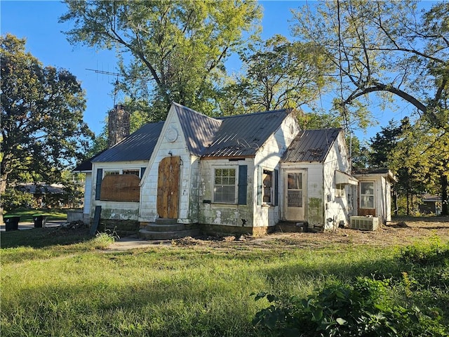 view of front of home with entry steps, metal roof, a chimney, and a front yard