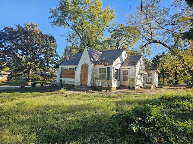 view of front of house with entry steps, metal roof, central air condition unit, a front lawn, and a chimney