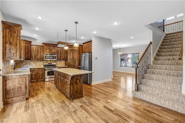 kitchen with a kitchen island, light hardwood / wood-style flooring, stainless steel appliances, sink, and decorative light fixtures