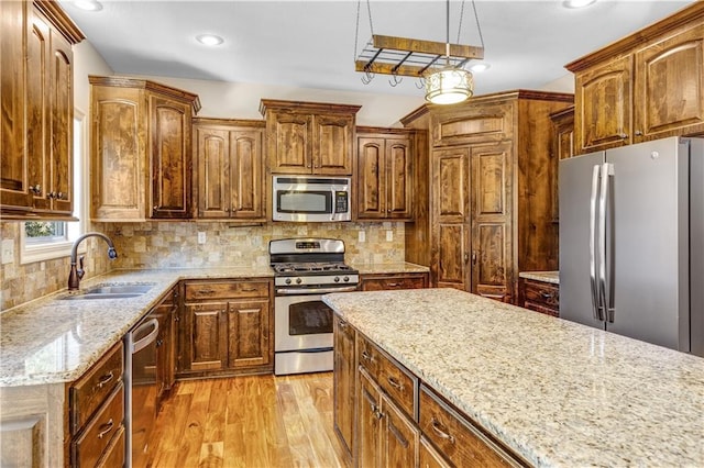 kitchen featuring light hardwood / wood-style flooring, hanging light fixtures, sink, appliances with stainless steel finishes, and tasteful backsplash