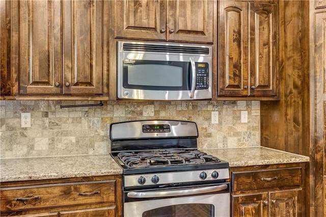 kitchen featuring light stone countertops, backsplash, and appliances with stainless steel finishes