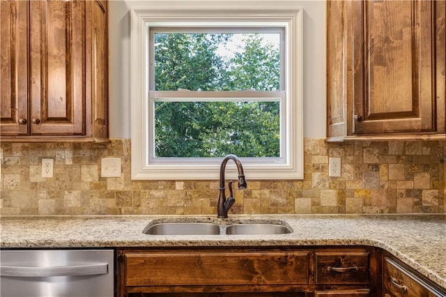 kitchen featuring stainless steel dishwasher, decorative backsplash, sink, and light stone counters