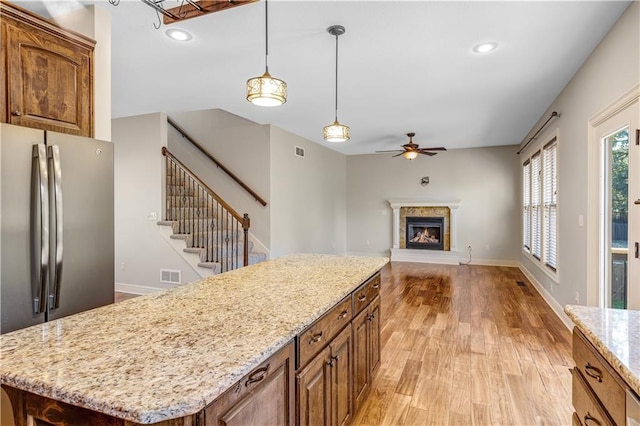 kitchen featuring a kitchen island, hanging light fixtures, light stone countertops, light hardwood / wood-style floors, and stainless steel refrigerator