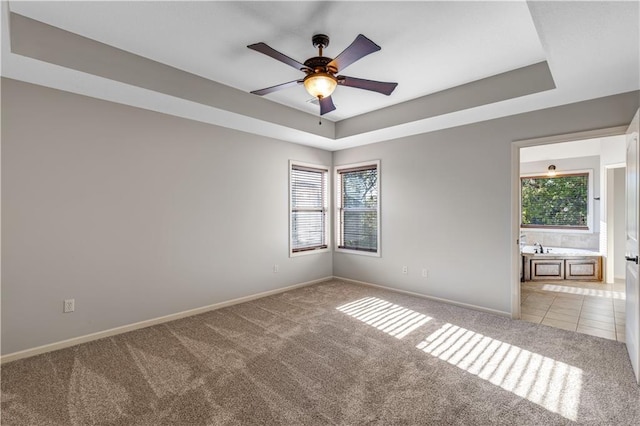 carpeted empty room with ceiling fan and a tray ceiling