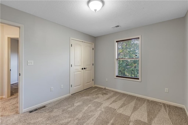 unfurnished bedroom featuring light carpet, a textured ceiling, and a closet