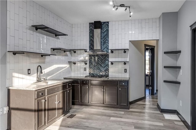 kitchen featuring wall chimney range hood, light hardwood / wood-style flooring, sink, light stone countertops, and dark brown cabinetry