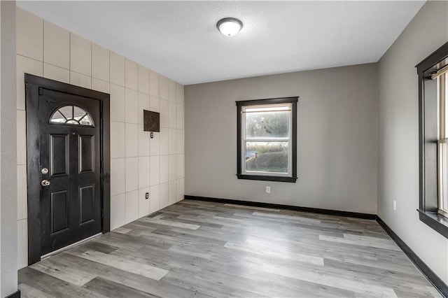 foyer entrance featuring light hardwood / wood-style flooring, a textured ceiling, and tile walls