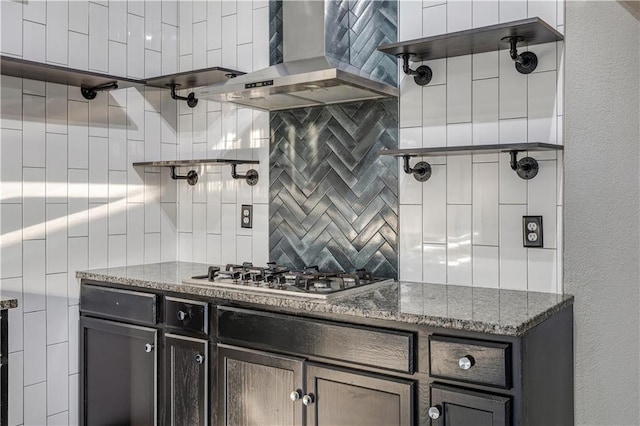 kitchen featuring wall chimney range hood, dark stone counters, decorative backsplash, and stainless steel gas stovetop