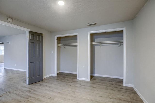 unfurnished bedroom with two closets, light hardwood / wood-style flooring, and a textured ceiling