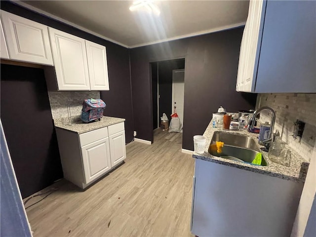 kitchen featuring light hardwood / wood-style floors, backsplash, sink, and white cabinetry