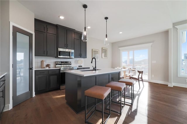 kitchen featuring pendant lighting, a center island with sink, appliances with stainless steel finishes, and dark hardwood / wood-style flooring