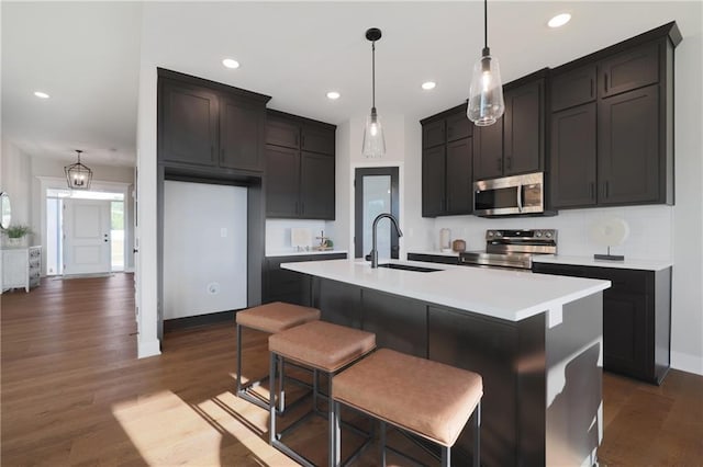 kitchen featuring an island with sink, stainless steel appliances, dark wood-type flooring, and sink