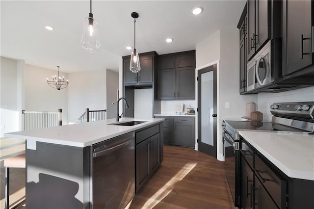 kitchen with dark hardwood / wood-style flooring, decorative light fixtures, sink, stainless steel appliances, and an island with sink