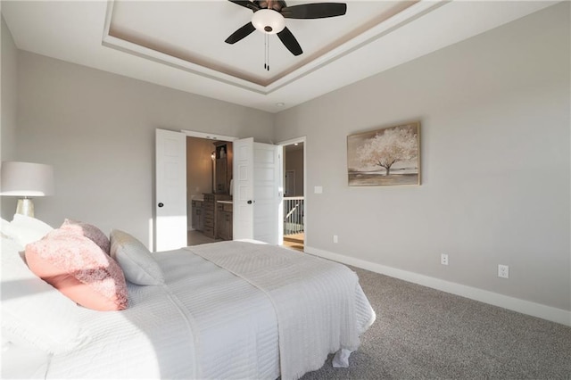 carpeted bedroom with ceiling fan, a raised ceiling, and ensuite bath