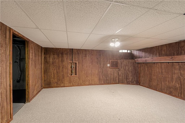 basement with light colored carpet, a paneled ceiling, and wooden walls