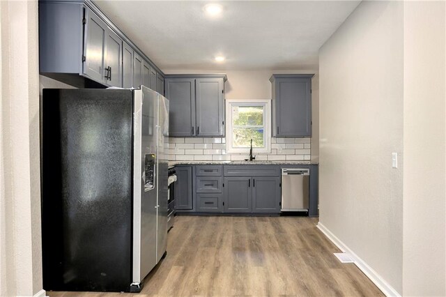 kitchen with sink, hardwood / wood-style floors, gray cabinets, appliances with stainless steel finishes, and tasteful backsplash