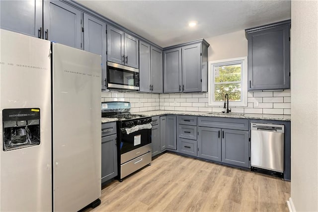 kitchen with light hardwood / wood-style floors, tasteful backsplash, stainless steel appliances, and sink