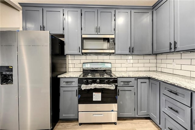 kitchen featuring backsplash, appliances with stainless steel finishes, gray cabinetry, light hardwood / wood-style floors, and light stone counters