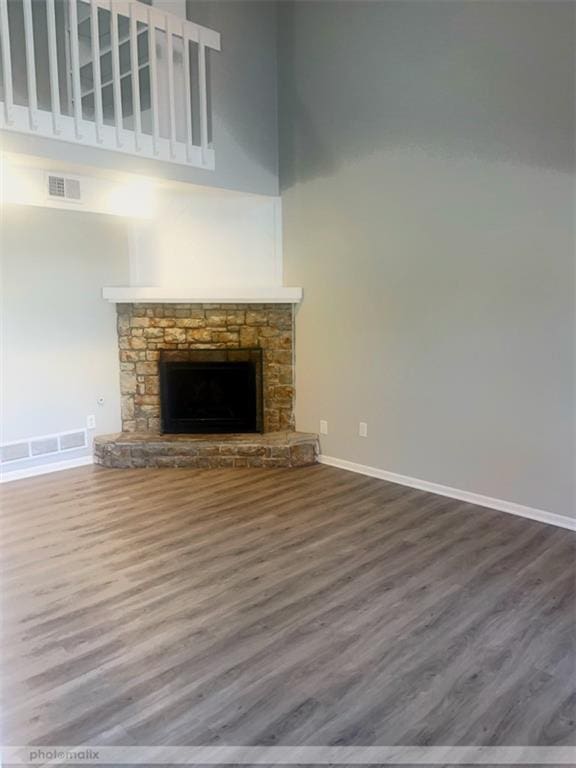 unfurnished living room with a stone fireplace, hardwood / wood-style floors, and a high ceiling