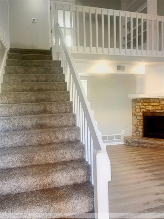 stairway with a fireplace, wood-type flooring, and a high ceiling