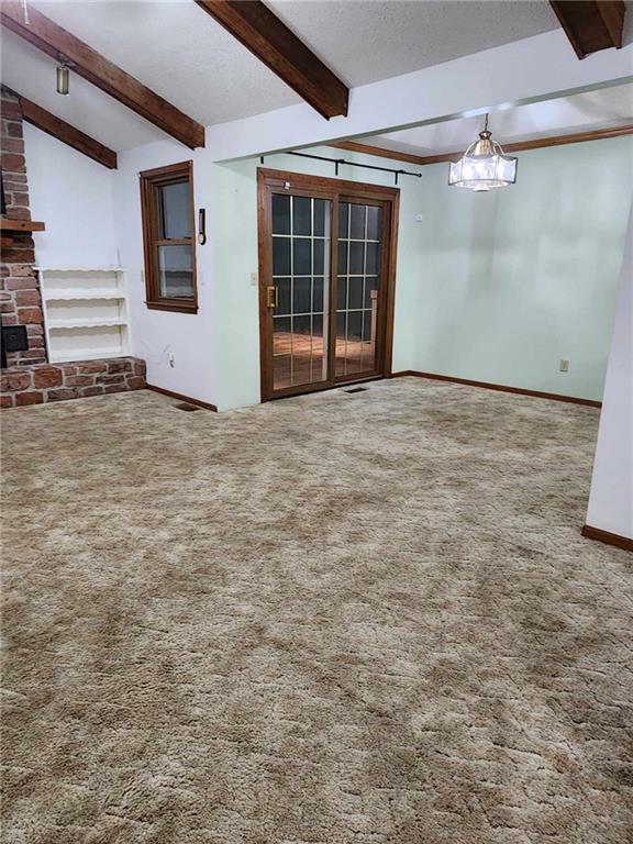 unfurnished living room with carpet flooring, a fireplace, beam ceiling, and a textured ceiling