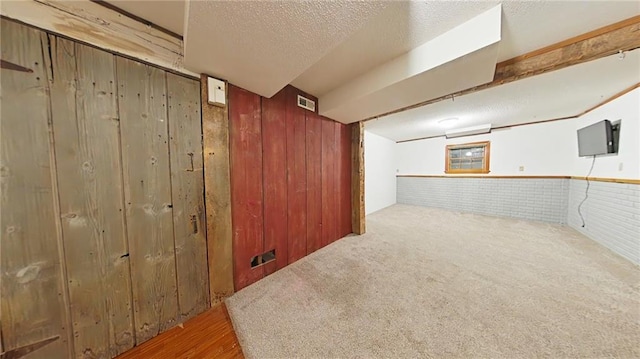 basement featuring a textured ceiling, carpet floors, and wooden walls